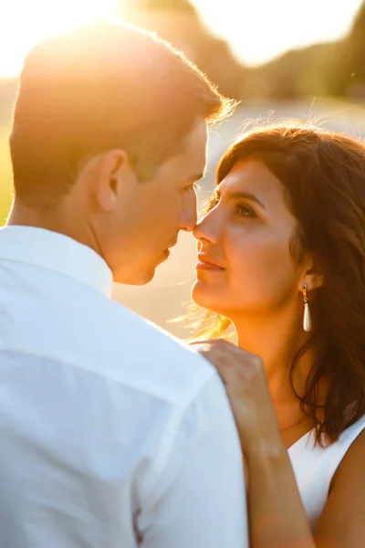 Lovely wedding couple at sunset. Bride and groom in wedding attire with a bouquet of flowers is in the hands against the backdrop of the green field at sunset. Romantic Married young family.