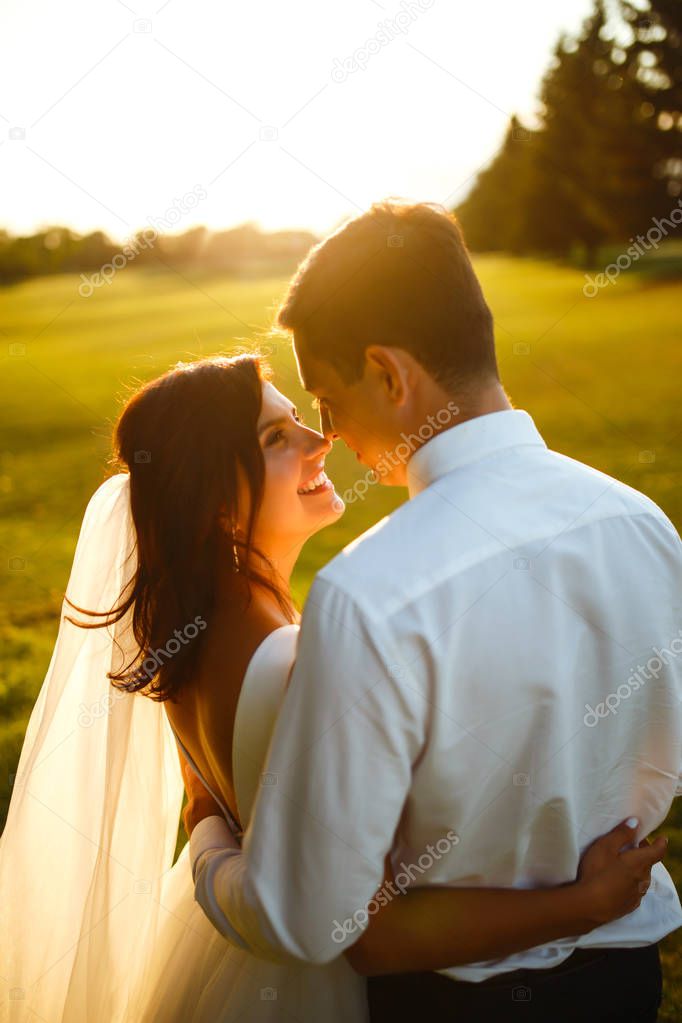 Lovely wedding couple at sunset. Bride and groom in wedding attire with a bouquet of flowers is in the hands against the backdrop of the green field at sunset. Romantic Married young family. 