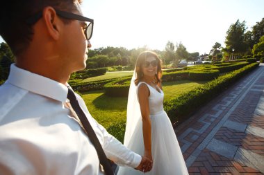 Evli çift eğleniyor. Şık bir takım elbise içinde damat ve güzel beyaz bir gelinlik içinde çift düğün günlerinde parkta yürüyorlar. Öpüşmek, eğlenmek, dans etmek, mutluluk.