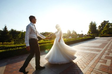 Evli çift eğleniyor. Şık bir takım elbise içinde damat ve güzel beyaz bir gelinlik içinde çift düğün günlerinde parkta yürüyorlar. Öpüşmek, eğlenmek, dans etmek, mutluluk.