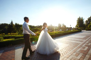 Evli çift eğleniyor. Şık bir takım elbise içinde damat ve güzel beyaz bir gelinlik içinde çift düğün günlerinde parkta yürüyorlar. Öpüşmek, eğlenmek, dans etmek, mutluluk.