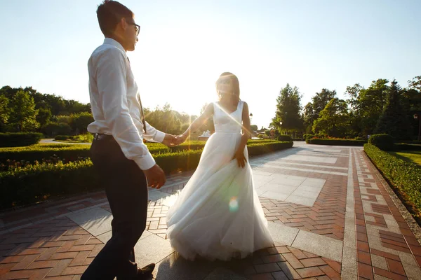 已婚夫妇玩得很开心 身着时髦西服的新郎和身穿漂亮白色礼服的新娘 在他们的婚礼当天正在公园里散步 — 图库照片