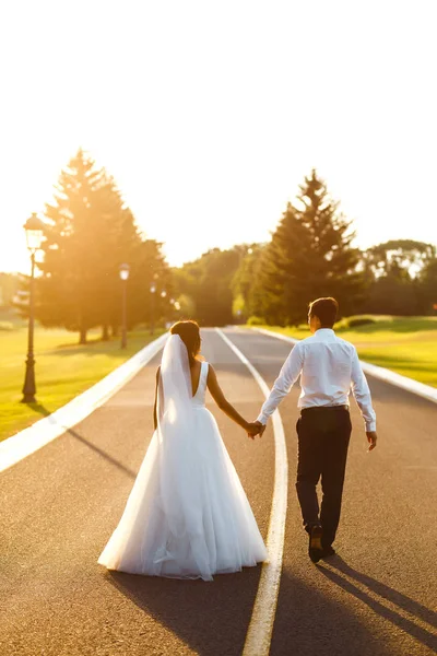 一对恋人携手并肩地走在路上迎接日落 一对新婚夫妇幸福地走在路上 从后面看 在一起 年轻的家庭 — 图库照片