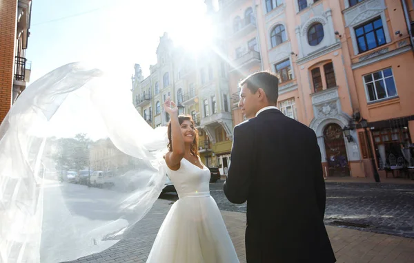 Bride and groom kisses tenderly in the shadow of a flying veil. A stylish bridegroom in a black suit gently embraces a beautiful bride in a white dress with a flying veil. Together. Wedding. Love.