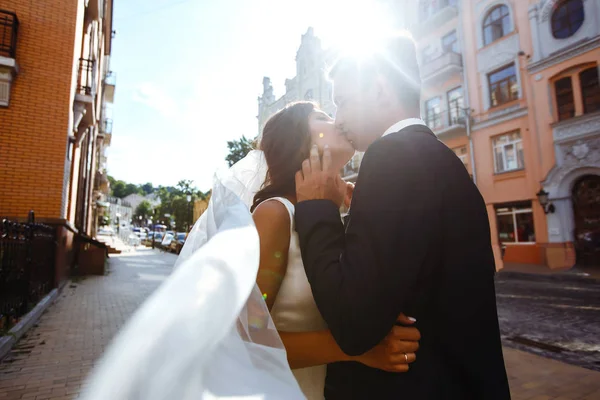 Bride and groom kisses tenderly in the shadow of a flying veil. A stylish bridegroom in a black suit gently embraces a beautiful bride in a white dress with a flying veil. Together. Wedding. Love.