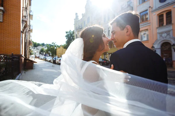 Bride and groom kisses tenderly in the shadow of a flying veil. A stylish bridegroom in a black suit gently embraces a beautiful bride in a white dress with a flying veil. Together. Wedding. Love.