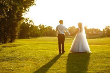 Mutlu gelin ve damat gün batımına gidiyor. Gün batımında harika bir çift. Gelin ve damat, gün batımında yeşil tarlanın arka planına karşı ellerinde olacak. Birlikte. Düğün.. 