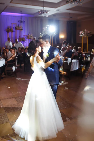 First wedding dance of newlywed. Groom holds bride\'s hand dancing with her in the middle of a restaurant. Touching and emotional first dance of the couple on their wedding with lights.