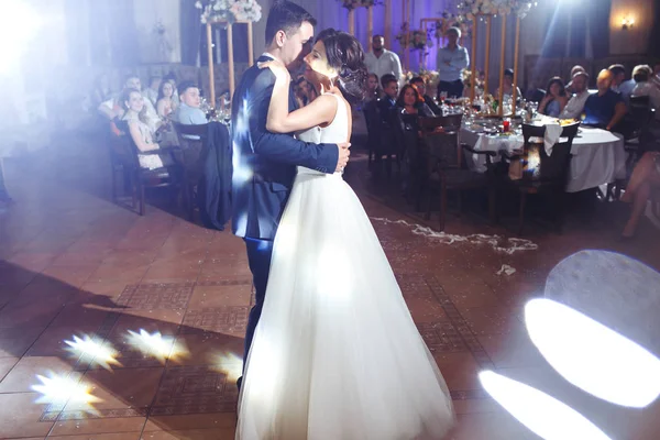 First wedding dance of newlywed. Groom holds bride's hand dancing with her in the middle of a restaurant. Touching and emotional first dance of the couple on their wedding with lights.