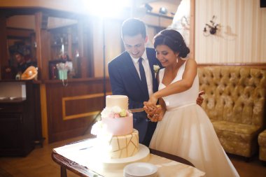 Mutlu gelin ve damat düğün ziyafetinde şık düğün pastalarını kesiyorlar. Yeni evliler ellerinde bıçakla çiçeklerle süslenmiş düğün pastasını kesiyorlar. Çiftler için tatlı pasta..