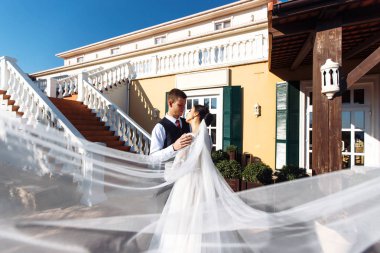 Yeni evliler, uçan bir duvağın gölgesinde şefkatle eğleniyorlar. Siyah takım elbiseli şık bir damat uçan peçeli beyaz elbiseli güzel bir gelini nazikçe kucaklıyor. Romantik an.