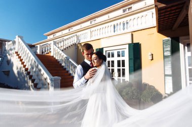 Yeni evliler, uçan bir duvağın gölgesinde şefkatle eğleniyorlar. Siyah takım elbiseli şık bir damat uçan peçeli beyaz elbiseli güzel bir gelini nazikçe kucaklıyor. Romantik an.