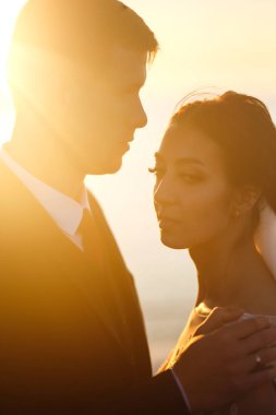 Güzel gelin ve şık damat gün batımında teknenin arka planına karşı köprüde yan yana. Yeni evliler gün batımında şefkatle sarılır, öpüşür ve eğlenirler. Düğün için. Sevgi. Romantik an. 