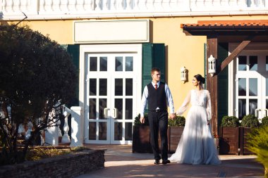 Yeni evliler şefkatle sarılır, öpüşür ve birbirlerinden hoşlanırlar. Aşıkların yürüyüşü. İnanılmaz gülümseyen bir düğün çifti. Güzel gelin ve şık damat. Romantik bir an. Sevgi. Birlikte. Düğün için. Evlilik..