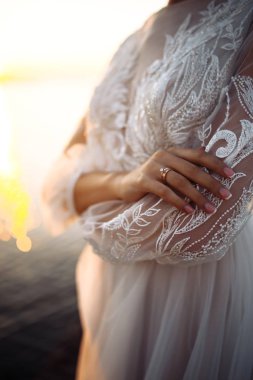 Nişan yüzüğü gelinin parmağında. Deniz ve günbatımının arka planında zarif bir alyans takmış beyaz elbiseli güzel bir gelin. Düğün günü. Düğün ayrıntılarını kavra.