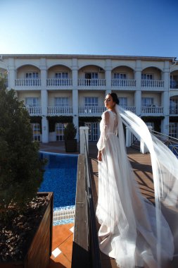 Havuz kenarında poz veren beyaz elbiseli güzel seksi gelin. Şatafatlı gelinlik içinde güneşin altında poz veren mutlu gelin. Rüzgar duvağını açıyor. Düğün günü. Evlilikten. Moda Gelini.