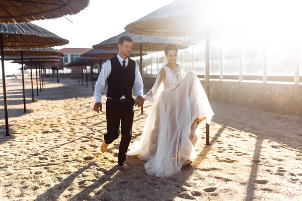 美丽的新娘和新郎手牵着手在沙滩上漫步 在海滩上相爱的新婚夫妇 新娘和新郎在海滩与浪漫的时刻 在一起 年轻的家庭 — 图库照片