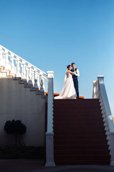 新娘和新郎在楼梯的台阶上 优雅时尚的年轻夫妇拥抱在一起 在楼梯上享受彼此 新婚夫妇在户外的楼梯上摆姿势谈恋爱 在一起 — 图库照片