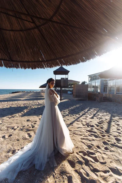 美丽的新娘穿着白衣 沐浴在阳光下沿着沙滩散步 拥有奢华妆容和发型的快乐新娘 美丽的新娘在阳光和蓝天中 婚礼日 — 图库照片