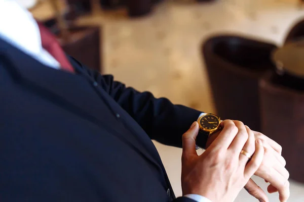 Stylish men's wrist watch, the man is watching the time. Businessman clock, businessman checking time on his wristwatch. Groom's hands in a  dark suit adjusting wristwatch.