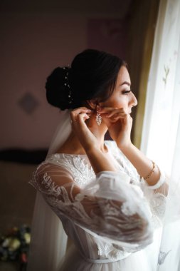 Şık, mutlu gelin sabah hazırlanıyor. Mutlu yeni evli kadın yatak odasında. Profesyonel makyajlı ve saç stili olan güzel bir kadın. Gelinin sabahı. Düğün günü. Moda Gelini.