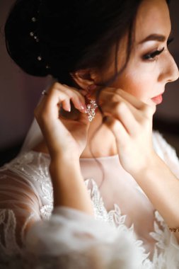 Şık, mutlu gelin sabah hazırlanıyor. Mutlu yeni evli kadın yatak odasında. Profesyonel makyajlı ve saç stili olan güzel bir kadın. Gelinin sabahı. Düğün günü. Moda Gelini.
