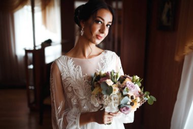 Düğün buketi olan güzel bir gelin. Profesyonel makyajlı ve saç stili olan güzel bir kadın. Şık, mutlu gelin sabah hazırlanıyor. Düğün günü. Moda Gelini.