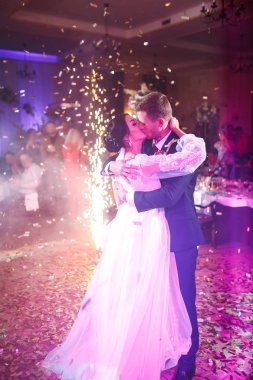 Yeni evlilerin ilk düğün dansı. Mutlu gelin ve damat ve arkaplanda renkli ışıklar ve konfeti ile şık bir restoranda ilk dansları. Düğün günü. Birlikte