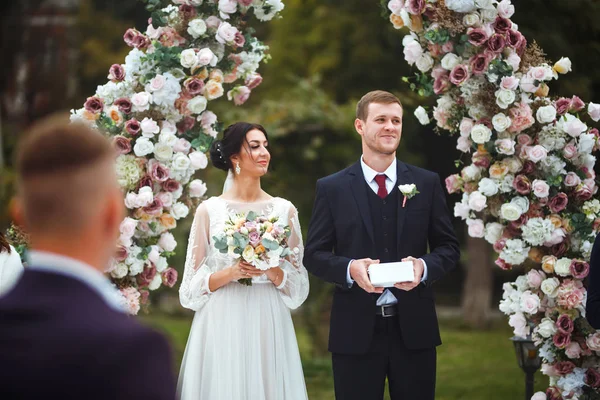 在一个用鲜花装饰的拱门下举行的婚礼上 新郎和新娘都很快乐 婚礼上两个情人的心 美丽的新娘和时尚的新郎 婚礼的日子 一起来 — 图库照片