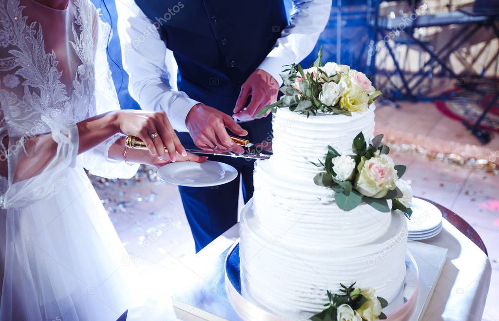 Elegant and stylish wedding cake with flowers. Newlyweds standing near a large wedding cake. Bride and a groom is cutting their wedding cake on wedding banquet in restaurant. Marriage. Together.