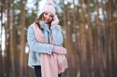 Genç ve güzel bir kadın ormanda gülüyor ve eğleniyor. Kız mavi bir ceket, örgü bir şapka, atkı ve eldiven giyiyor. Ormanda mutlu kış zamanları. Kutlama kavramı, Noel.