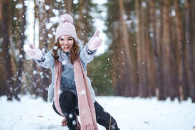Tatlı genç bir kadın ormanda karla oynuyor. Kız mavi bir ceket giymiş, örgü şapka, atkı ve eldiven takmış. Kış yaşam tarzı mutluluk, doğa. Noel, Yeni Yıl.