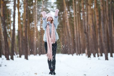 Tatlı genç bir kadın ormanda karla oynuyor. Kız mavi bir ceket giymiş, örgü şapka, atkı ve eldiven takmış. Kış yaşam tarzı mutluluk, doğa. Noel, Yeni Yıl.