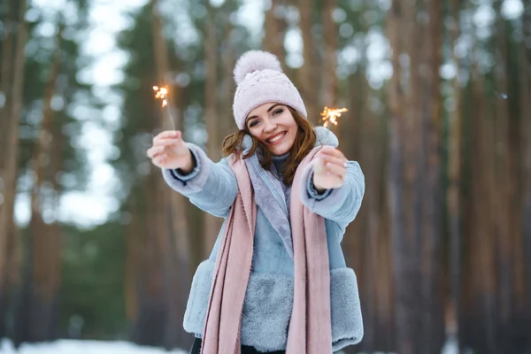 キラキラした女の子が手に持っている キラキラとポーズをとったニット帽姿の幸せなかわいい女の子 女の幸せと花火を再生します 森の中で幸せな冬の時間 クリスマスだ新年 — ストック写真