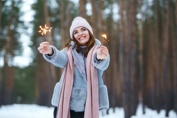 キラキラした女の子が手に持っている キラキラとポーズをとったニット帽姿の幸せなかわいい女の子 女の幸せと花火を再生します 森の中で幸せな冬の時間 クリスマスだ新年 — ストック写真