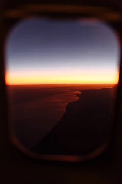 Beautiful scenic view through the aircraft window at sunset or sunrise time. Window view from passenger seat  airplane. Flying above the clouds. Panorama high above city. Vacation and travel concept.