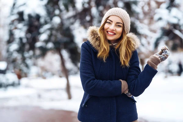 在冬天的森林里 美丽的女人站在雪树中间 年轻姑娘穿着蓝色夹克 头戴针织帽子 头戴手套 冬天快乐 在冬季公园里的时髦的年轻女子 圣诞节 — 图库照片
