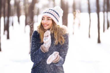 Mutlu genç kadın güneşli kış gününde karla oynuyor. Kızlar kışı sever, dondurucu günü. Kış tatillerinde karla oynayan bir kadın, havaya beyaz kar fırlatır. Kış ormanlarında yürü.