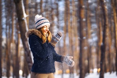 Mutlu genç kadın güneşli kış gününde karla oynuyor. Kızlar kışı sever, dondurucu günü. Kış tatillerinde karla oynayan bir kadın, havaya beyaz kar fırlatır. Kış ormanlarında yürü.
