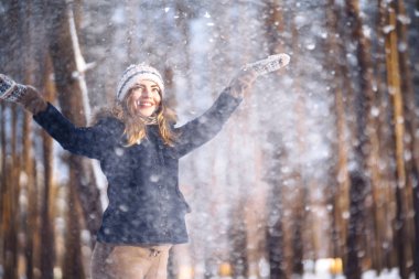 Mutlu genç kadın güneşli kış gününde karla oynuyor. Kızlar kışı sever, dondurucu günü. Kış tatillerinde karla oynayan bir kadın, havaya beyaz kar fırlatır. Kış ormanlarında yürü.