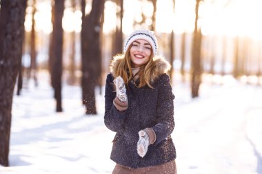 Mutlu genç kadın güneşli kış gününde karla oynuyor. Kızlar kışı sever, dondurucu günü. Kış tatillerinde karla oynayan bir kadın, havaya beyaz kar fırlatır. Kış ormanlarında yürü.