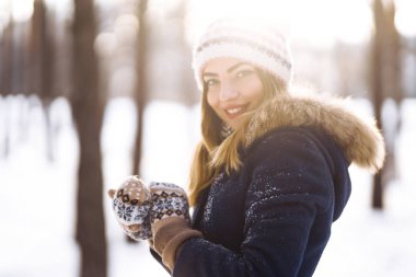 Uzun saçlı, mavi ceketli, örgü şapkalı ve eldivenli güneşli kış gününde poz veren güzel bir kızın portresi. Kış ormanlarında moda genç kadın. Noel, kış tatili konsepti. 