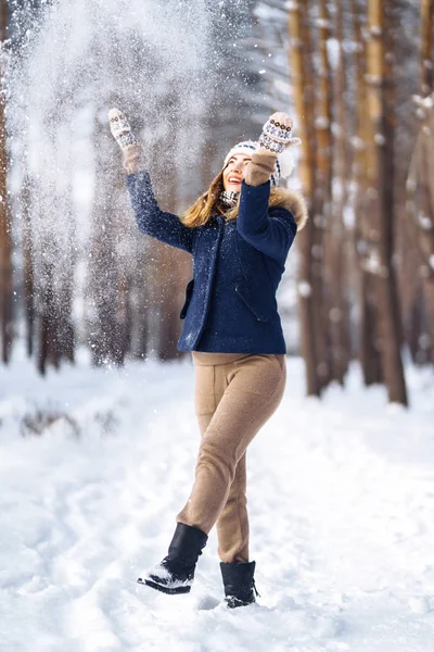 Happy young woman plays with a snow in sunny winter day. Girl enjoys winter, frosty day.  Playing with snow on winter holidays, a woman throws white, loose snow into the air. Walk in winter forest.