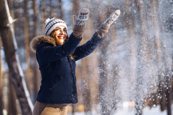 Happy young woman plays with a snow in sunny winter day. Girl enjoys winter, frosty day.  Playing with snow on winter holidays, a woman throws white, loose snow into the air. Walk in winter forest.