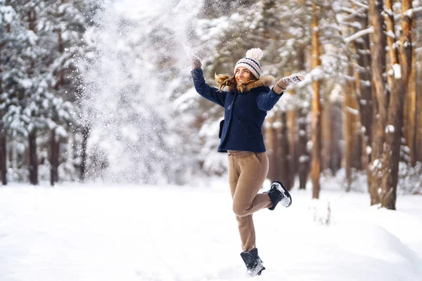 Happy young woman plays with a snow in sunny winter day. Girl enjoys winter, frosty day.  Playing with snow on winter holidays, a woman throws white, loose snow into the air. Walk in winter forest.