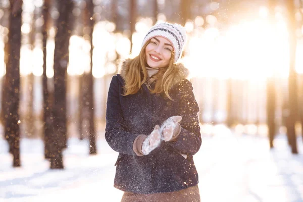 Happy young woman plays with a snow in sunny winter day. Girl enjoys winter, frosty day.  Playing with snow on winter holidays, a woman throws white, loose snow into the air. Walk in winter forest.