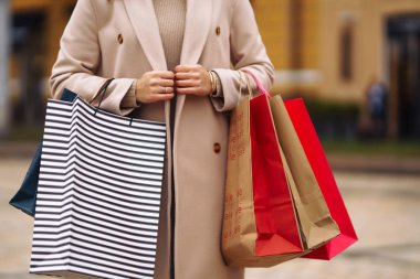 Alışveriş torbaları ellerde. Çok renkli çantaları ve alışverişleri olan genç bir kadının eli. Şehir caddesinde alışveriş torbaları tutan güzel bir kız. Tüketim, alışveriş, satış, yaşam tarzı konsepti. 