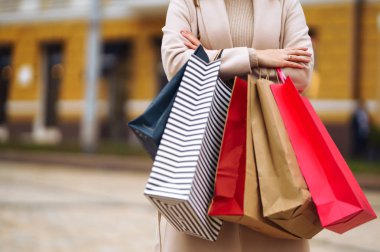 Alışveriş torbaları ellerde. Çok renkli çantaları ve alışverişleri olan genç bir kadının eli. Şehir caddesinde alışveriş torbaları tutan güzel bir kız. Tüketim, alışveriş, satış, yaşam tarzı konsepti. 