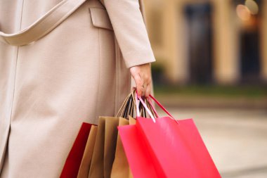 Alışveriş torbaları ellerde. Çok renkli çantaları ve alışverişleri olan genç bir kadının eli. Şehir caddesinde alışveriş torbaları tutan güzel bir kız. Tüketim, alışveriş, satış, yaşam tarzı konsepti. 
