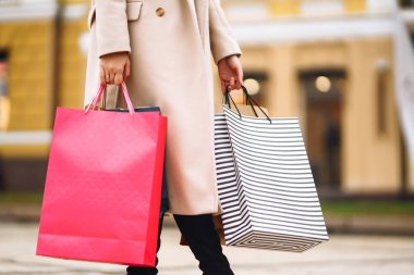 Alışveriş torbaları ellerde. Çok renkli çantaları ve alışverişleri olan genç bir kadının eli. Şehir caddesinde alışveriş torbaları tutan güzel bir kız. Tüketim, alışveriş, satış, yaşam tarzı konsepti. 